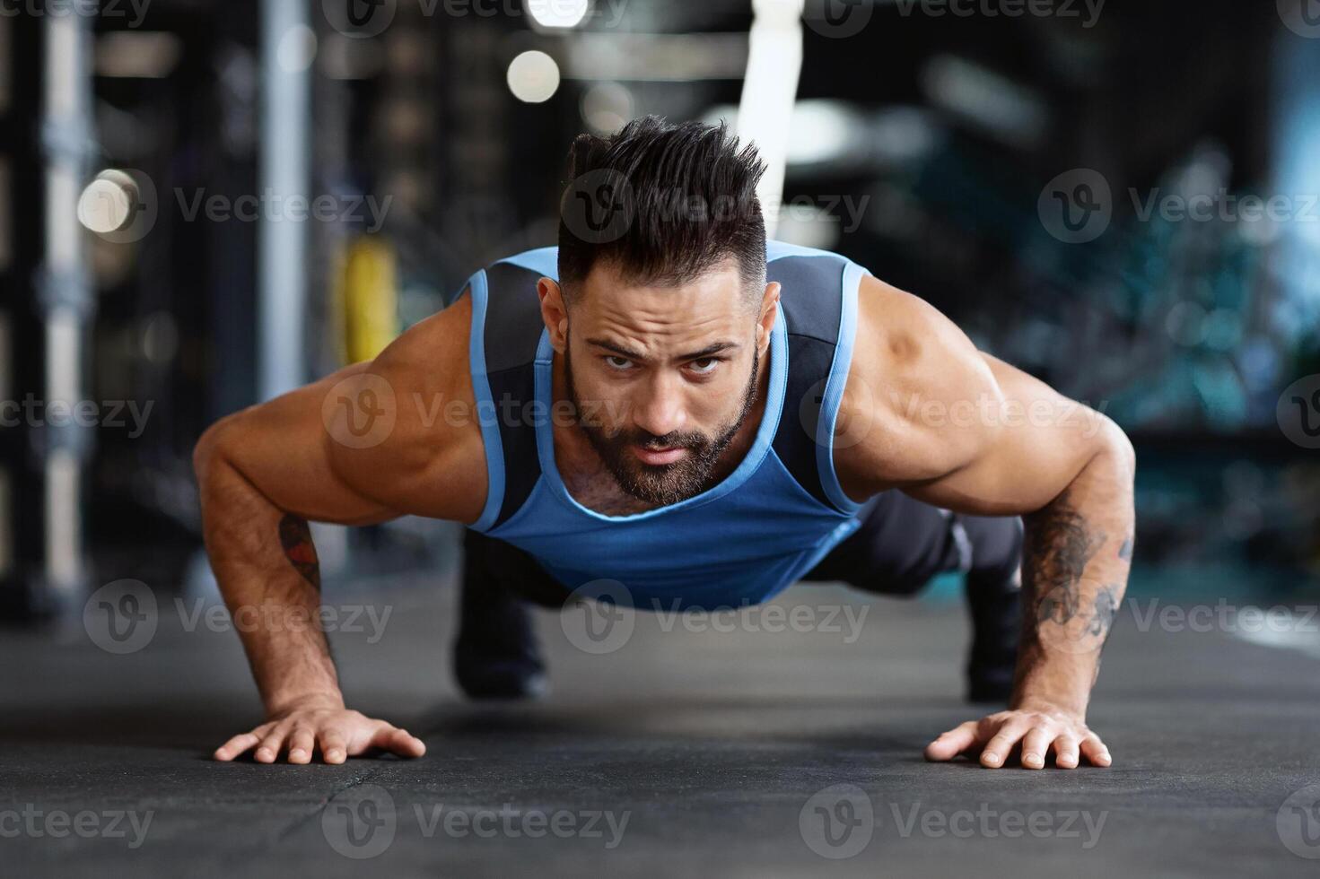 A man wearing a tank top does a push-up in a gym. photo