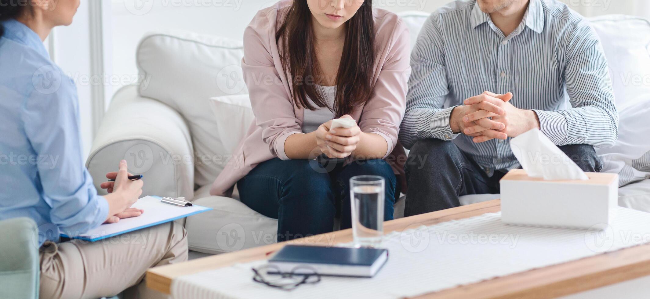 Cropped of couple is seated on a sofa during a counseling session with a therapist. They appear to be engaged in discussion, with the therapist taking notes photo