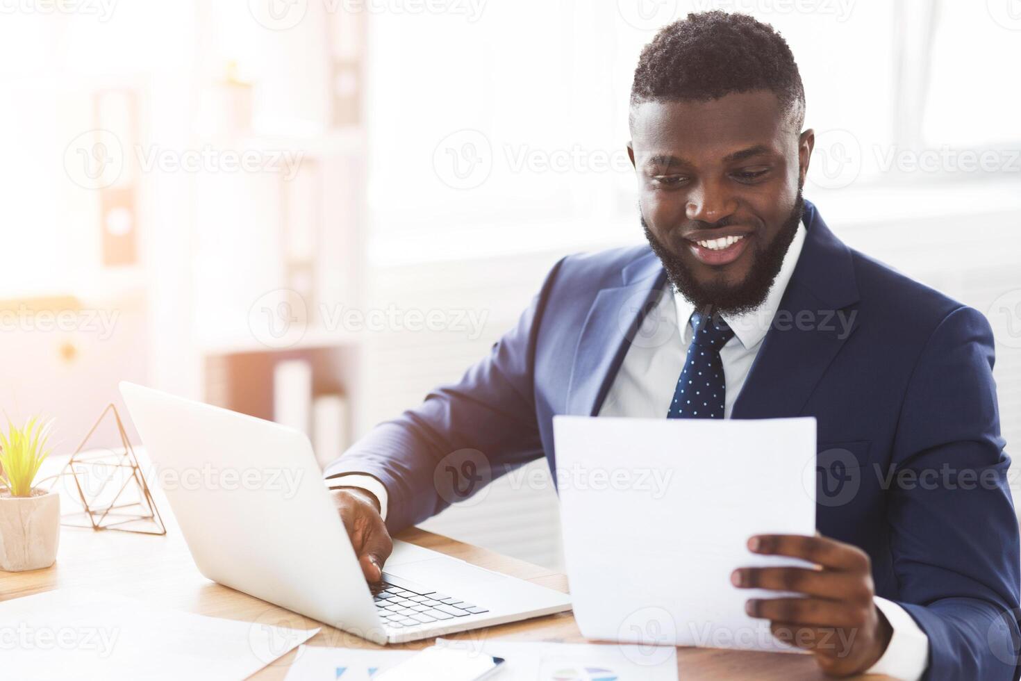 Satisfied african american businessman checking documents in modern office, side view, empty space photo