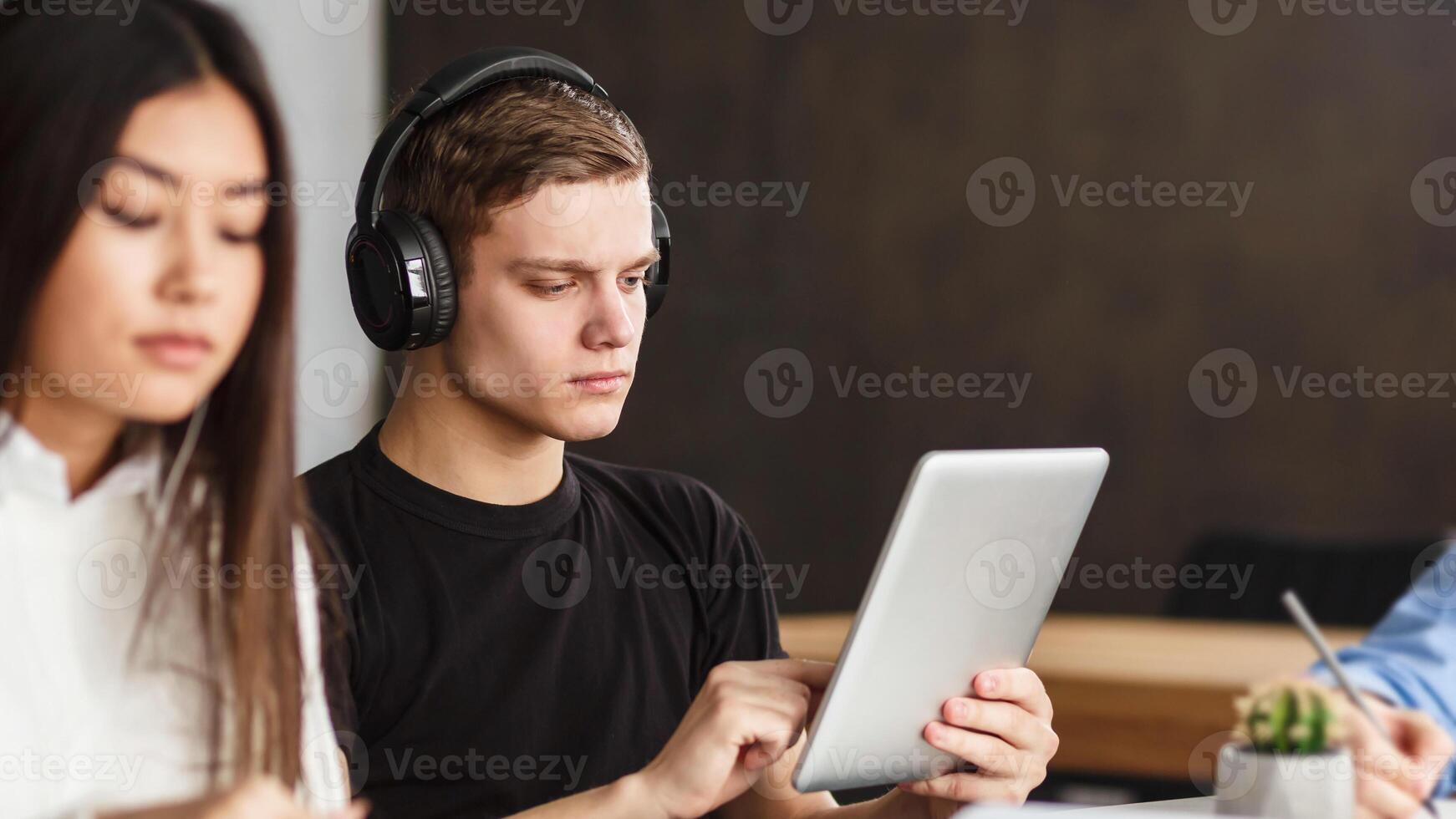 College student surfing internet on tablet in library, listening music in headphones, free space photo