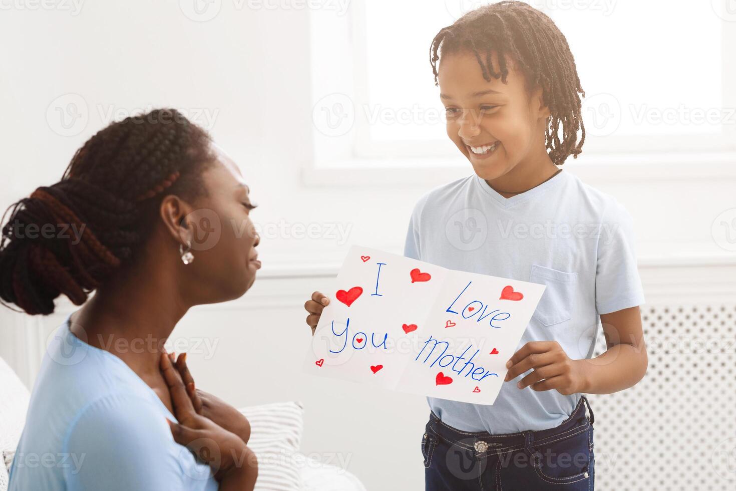 Touching Moment. African kid showing greeting card with I Love You, Mother text to her mom photo