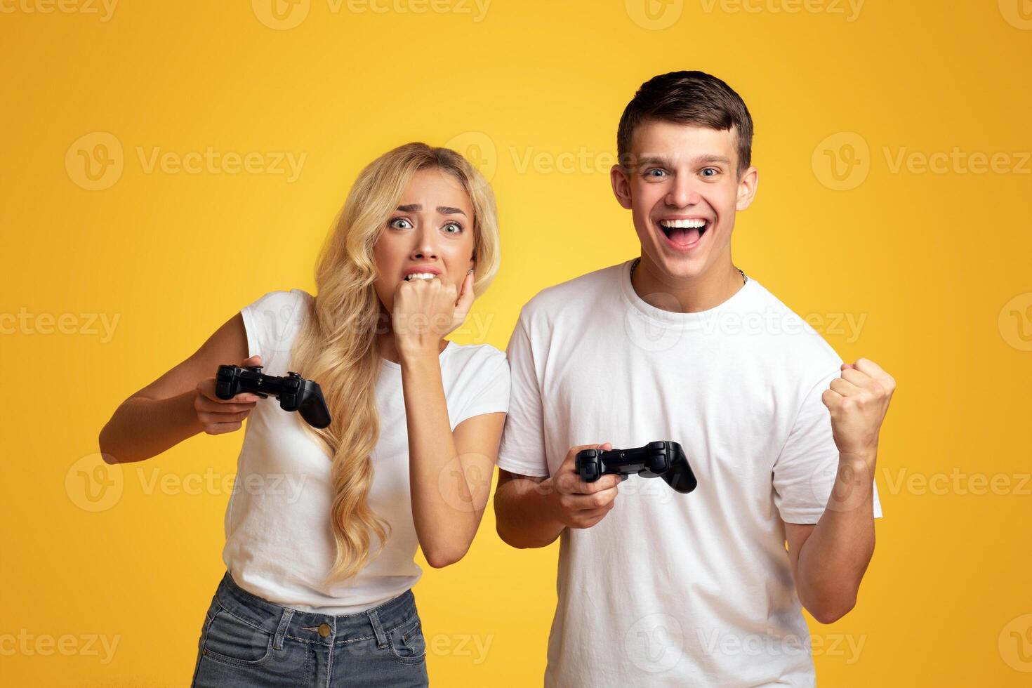 Gambling young couple playing game with joysticks, yellow studio background with empty space photo