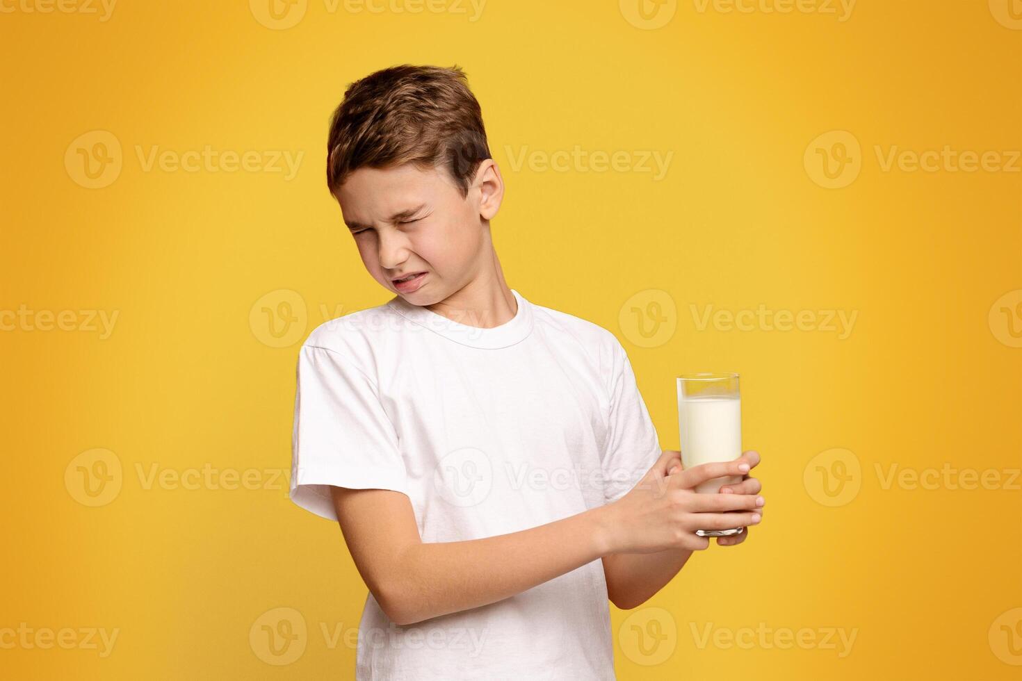 Lactose intolerance. Cute little boy does not want to drink milk, frowning on orange background photo