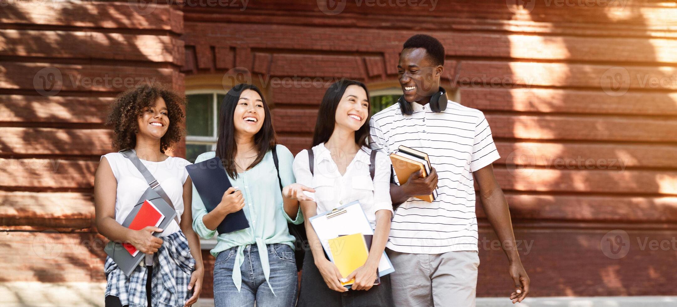 Group of happy students walking in university campus, chatting and laughing during break, copy space photo