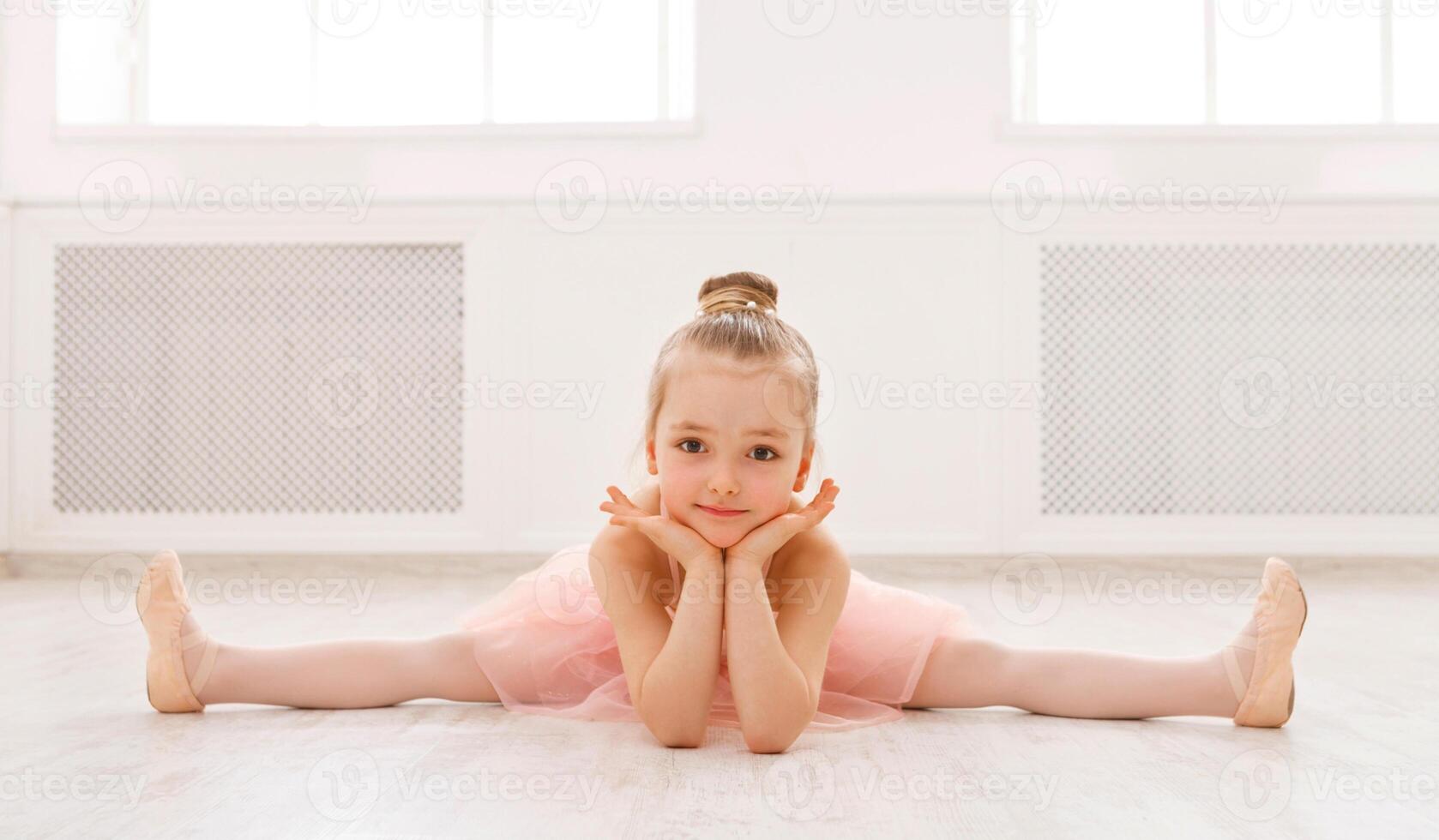 Little ballerina in split on floor, copy space. Smiling baby girl dreaming to become professional ballet dancer, classical dance school photo
