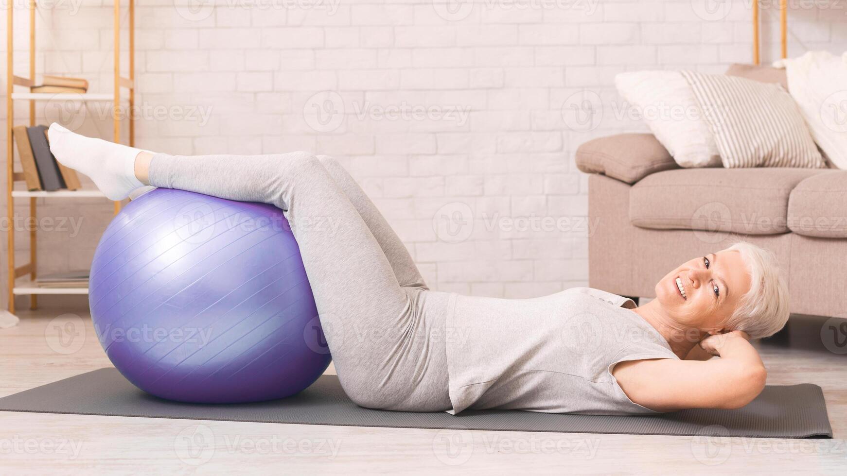 Elderly woman is engaging in a series of exercises on an exercise ball, balancing and working her core muscles. She is focused and determined, showcasing her strength and flexibility photo
