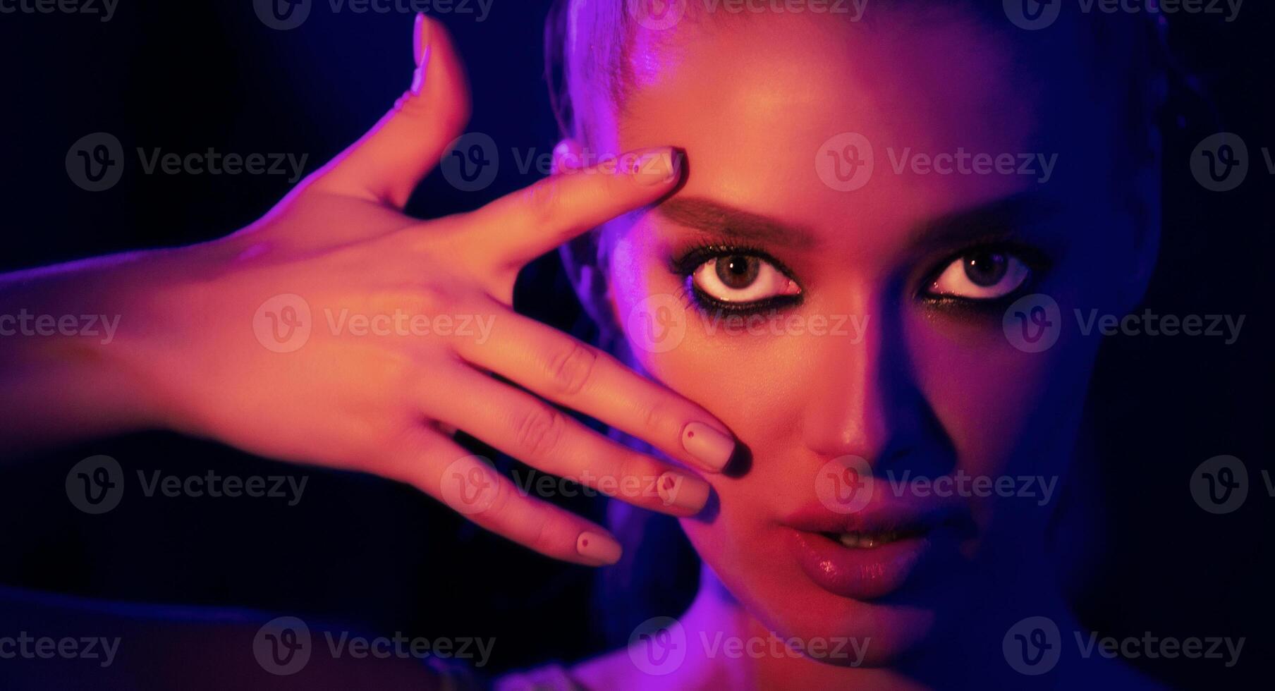 A woman is standing with her hand raised in front of her face, blocking her view. She appears to be shielding her eyes from the suns glare or possibly avoiding looking at something. photo