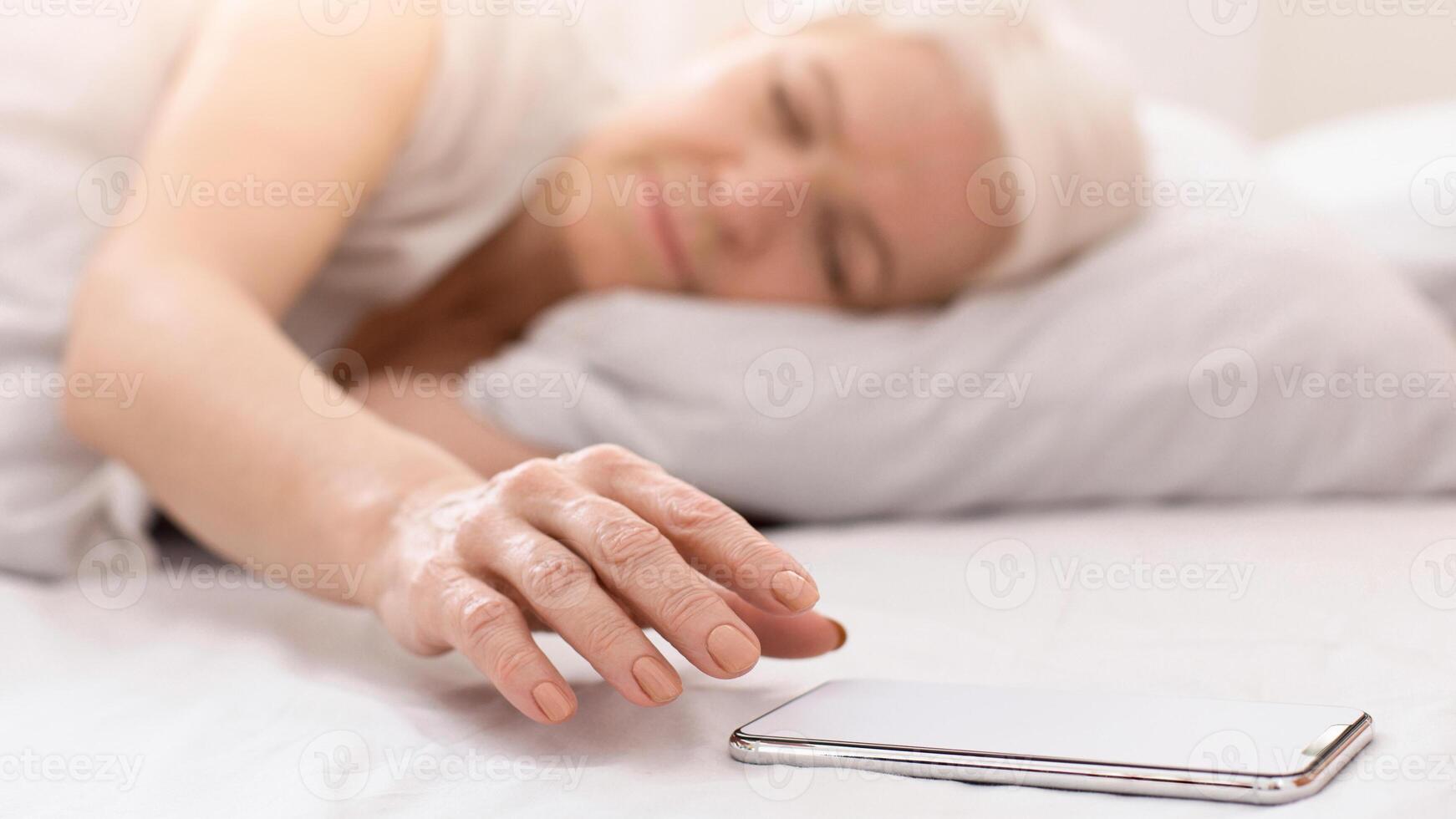 A woman is laying on a bed, staring at a cell phone in her hand. She seems engrossed in the screen, possibly texting or browsing. The room is dimly lit, creating a cozy atmosphere. photo