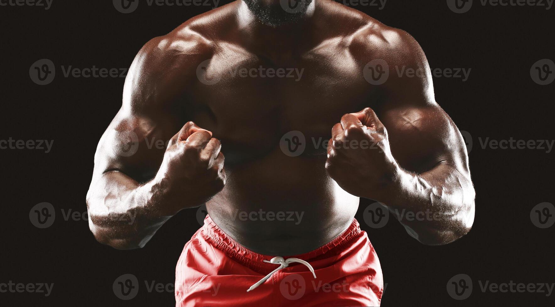A muscular man with dark skin is flexing his biceps against a black background, showcasing his impressive physique. photo