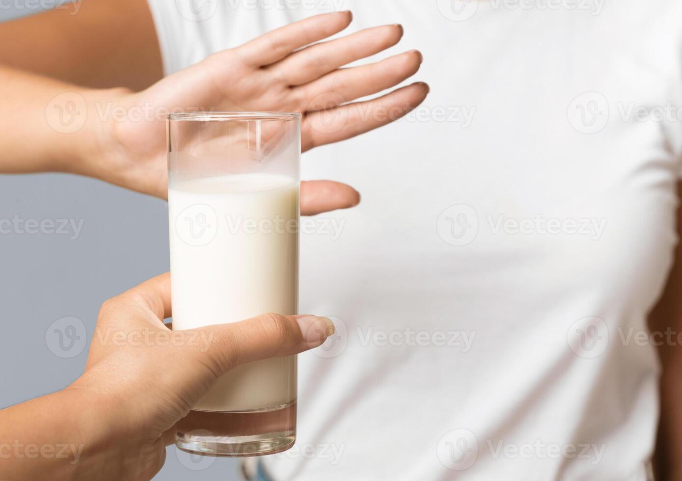 Unrecognizable Woman Gesturing No To Offered Glass Of Milk Standing In Studio On Gray Background. Cropped, Selective Focus photo