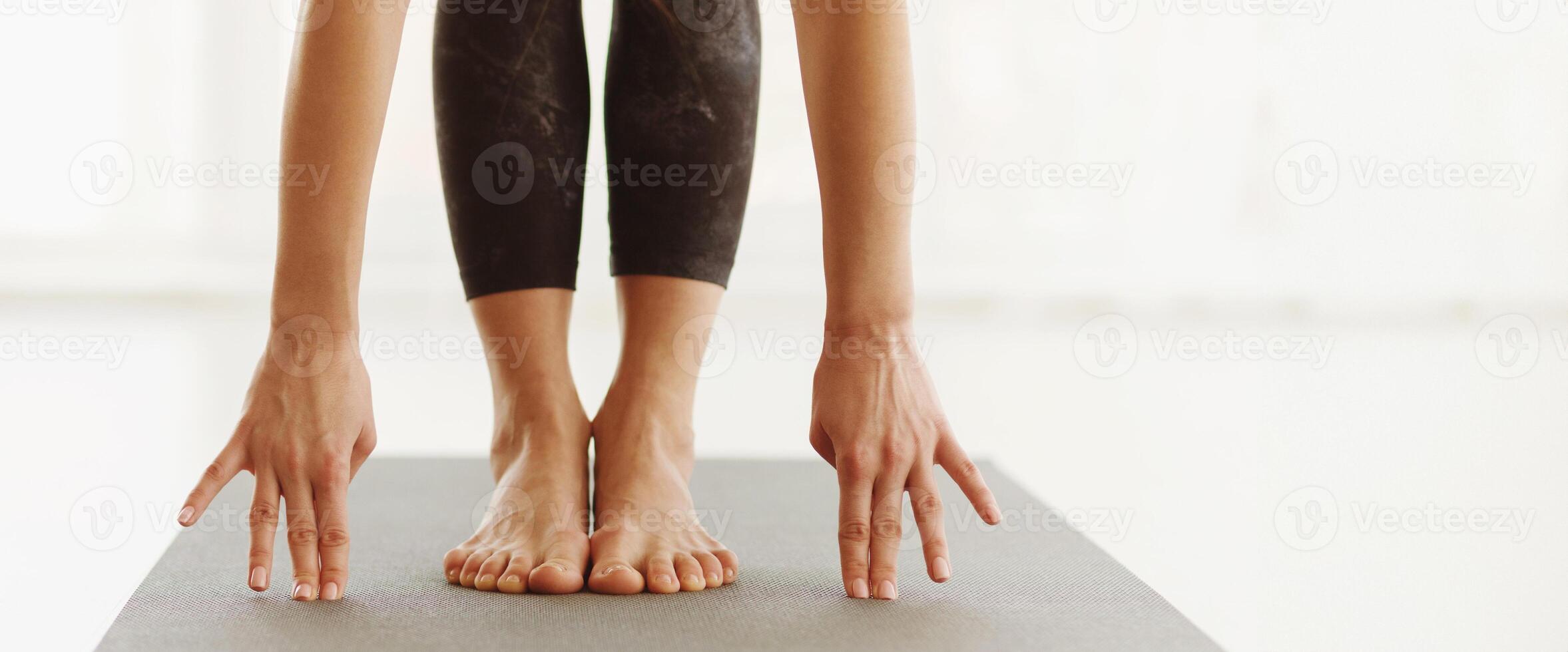 Lady is engaged in a yoga session indoors during the daytime, bending forward to touch their toes on a yoga mat, emphasizing flexibility and concentration, panorama with copy space photo