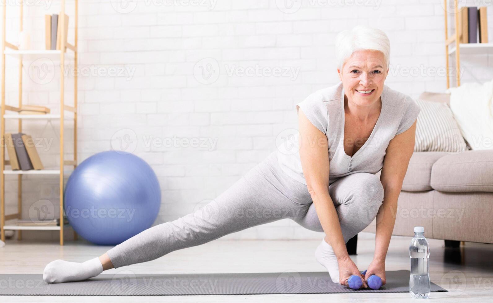 Active senior woman warming up, doing legs stretching exercises at home, panorama with empty space photo