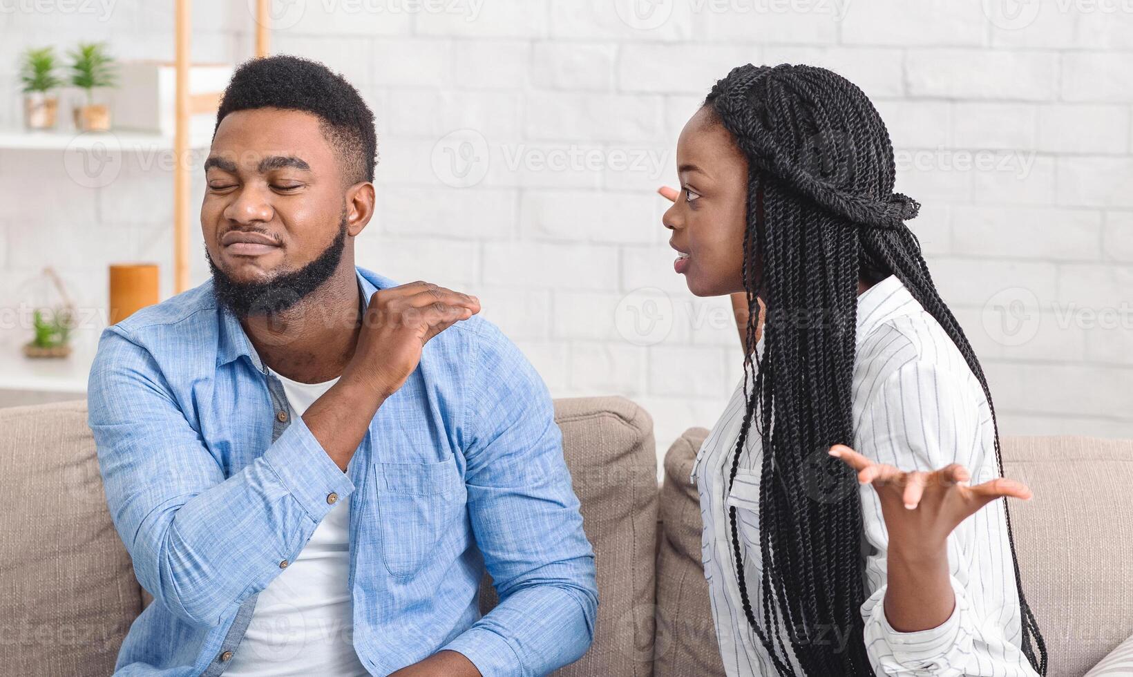 Family problems. Afro couple arguing at home, wife blaming husband while he is ignoring what she saying and showing bla bla bla gesture, panorama photo