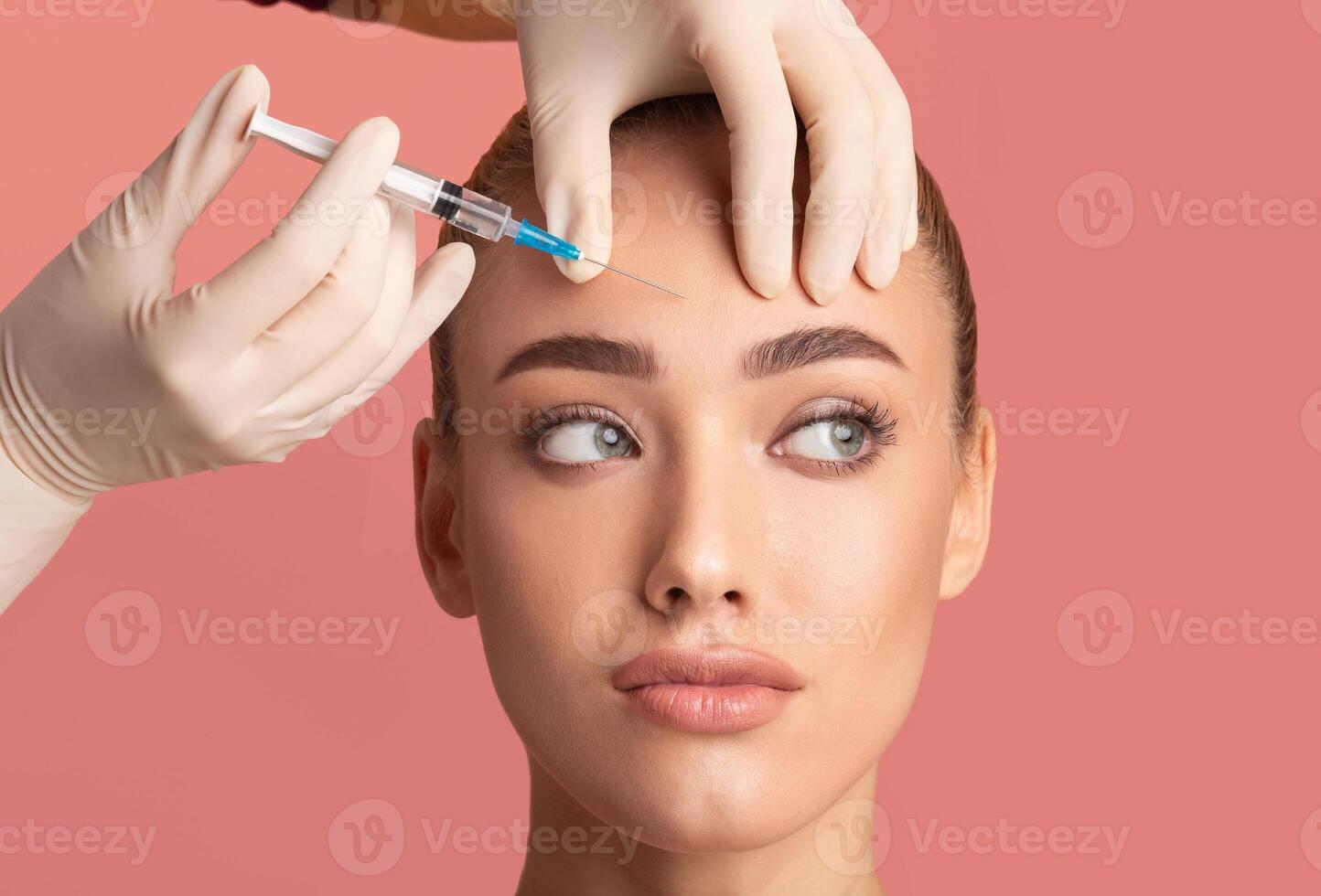 Skin Lifting Injection. Young Woman Receiving Botox Beauty Injection In Forehead Standing Over Pink Background. Studio Shot photo
