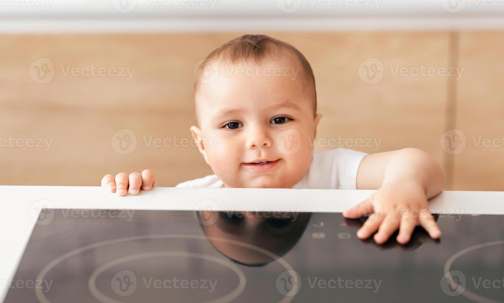 A cheerful baby reaches over a sleek kitchen counter, exploring their surroundings with a curious expression. The modern kitchen background enhances the innocence of the moment. photo