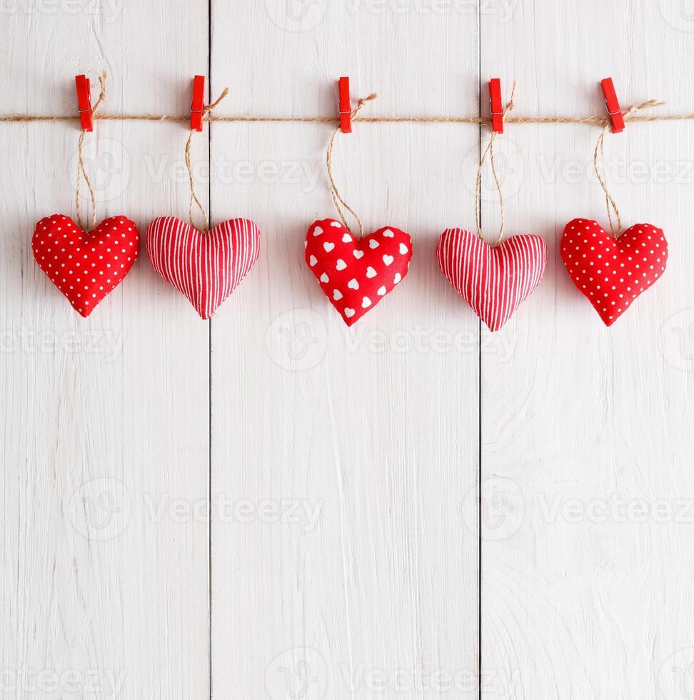 Valentine background with sewed pillow hearts row border on red clothespins at rustic white wood planks. Happy lovers day card mockup, copy space, vertical composition photo