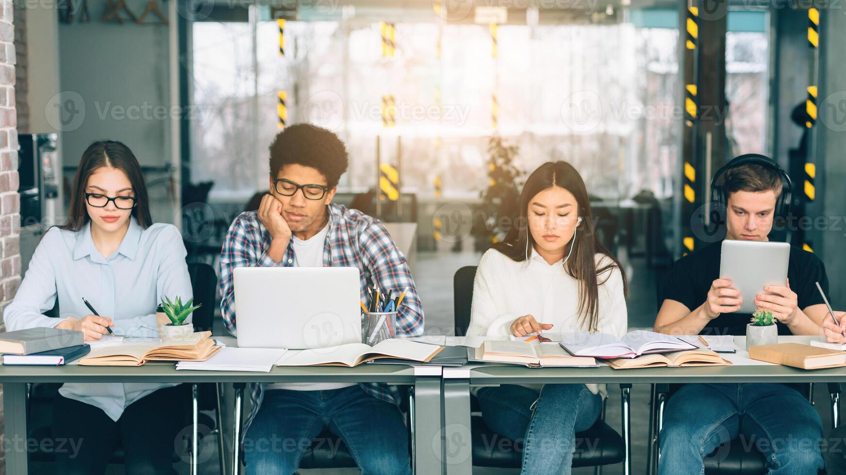 Serious students studying in college library with gadgets, preparing for final tests photo