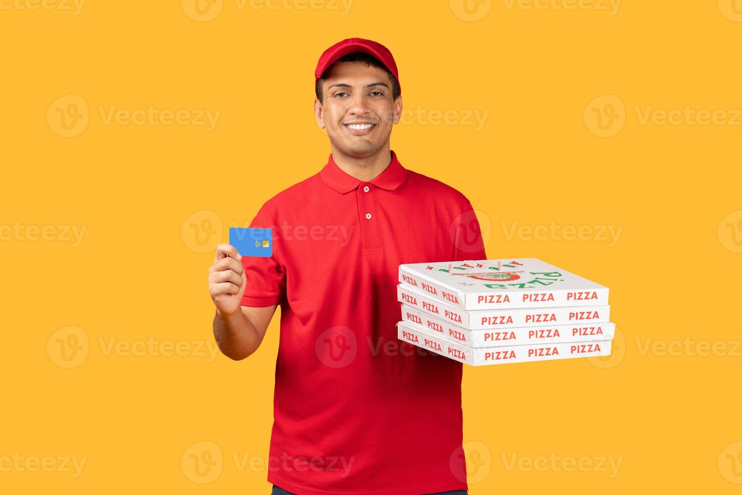Delivery man standing and holding a pizza box in one hand and a card in the other. He is dressed in red unform, yellow background photo