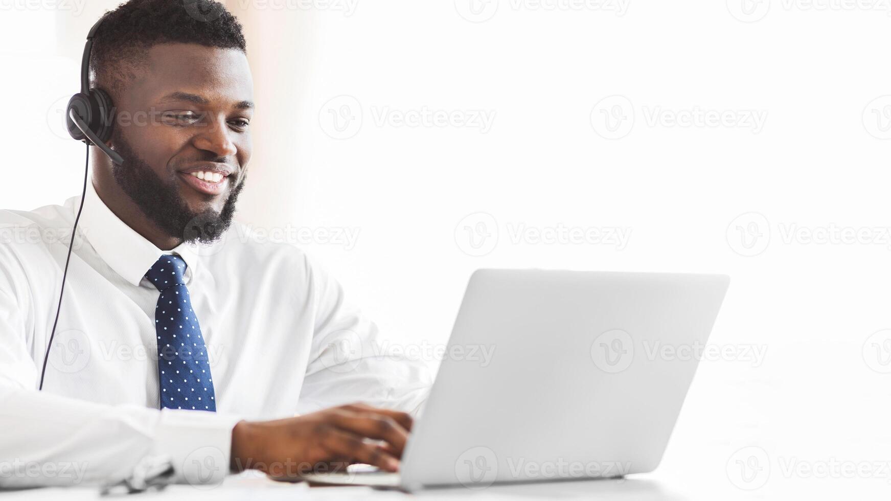 Young afro business consultant with headset typing email to client on laptop, empty space photo