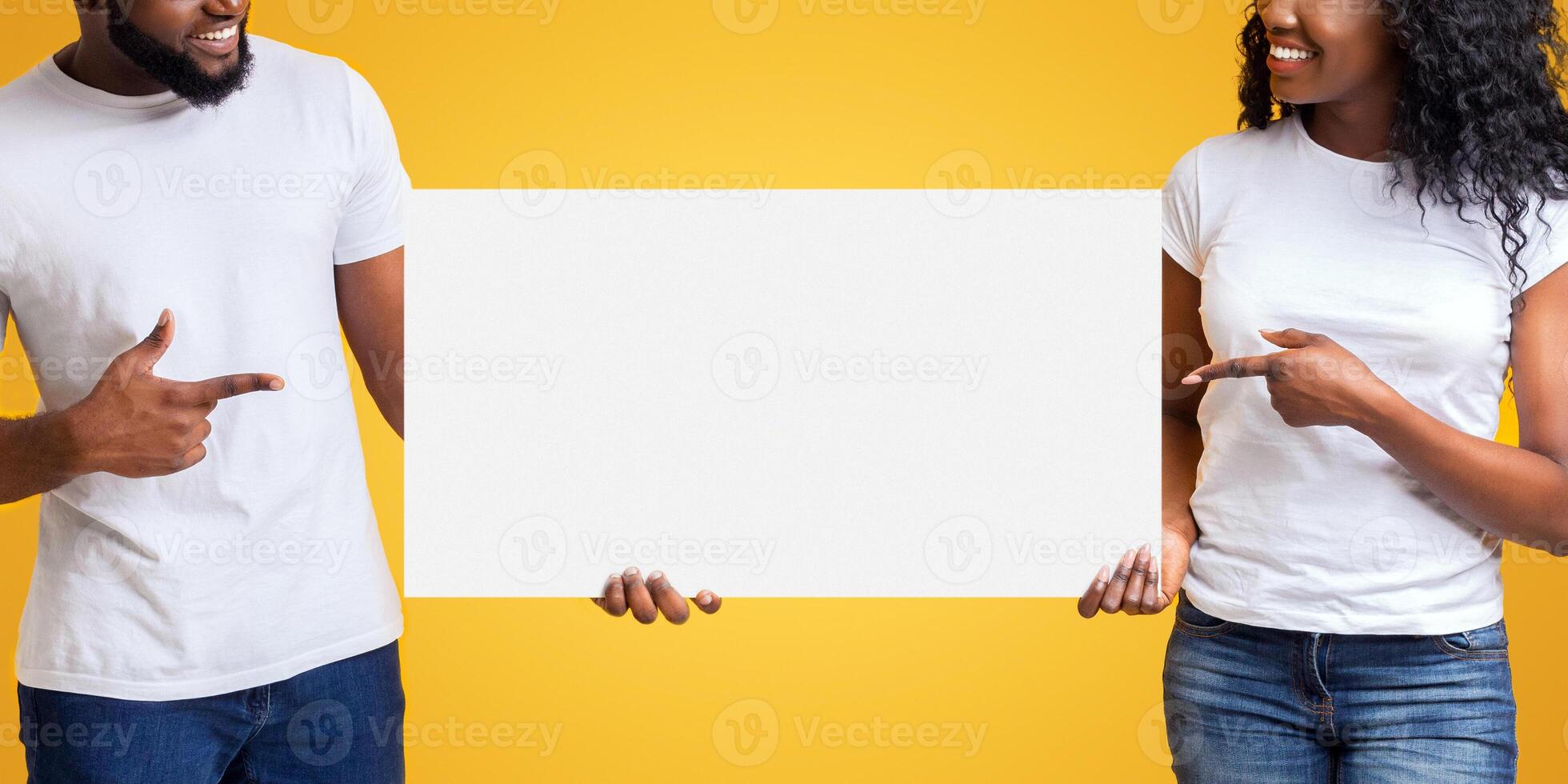 Black Smiling Couple Holding White Blank Card, pointing at blank, looking at board, yellow background photo