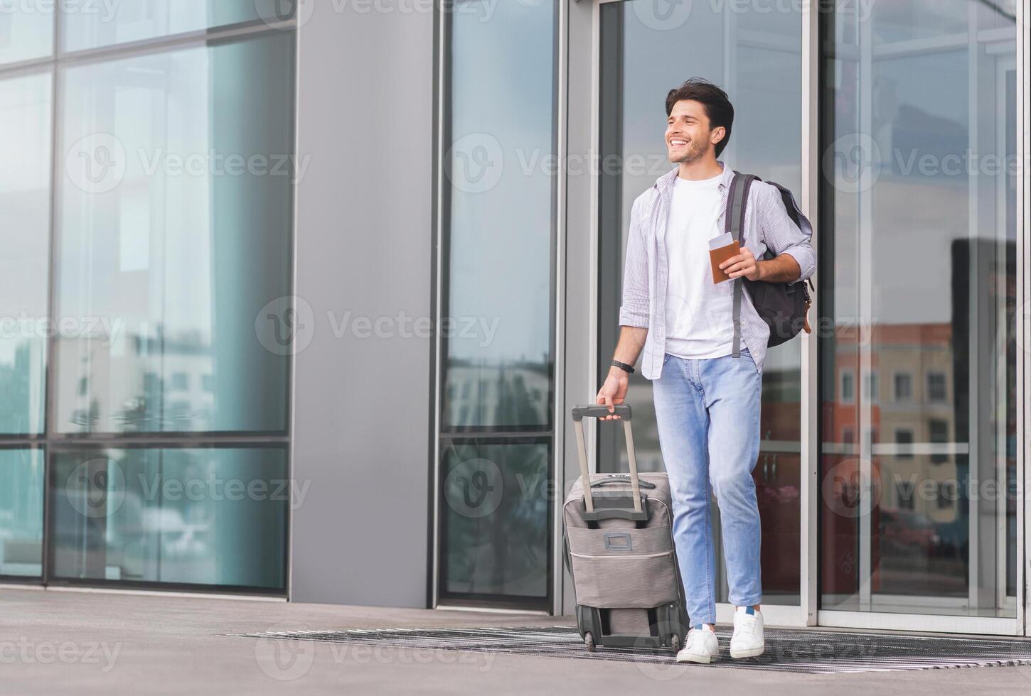 Enjoying long-awaited rest. Happy guy going out of airport building with luggage, copy space photo