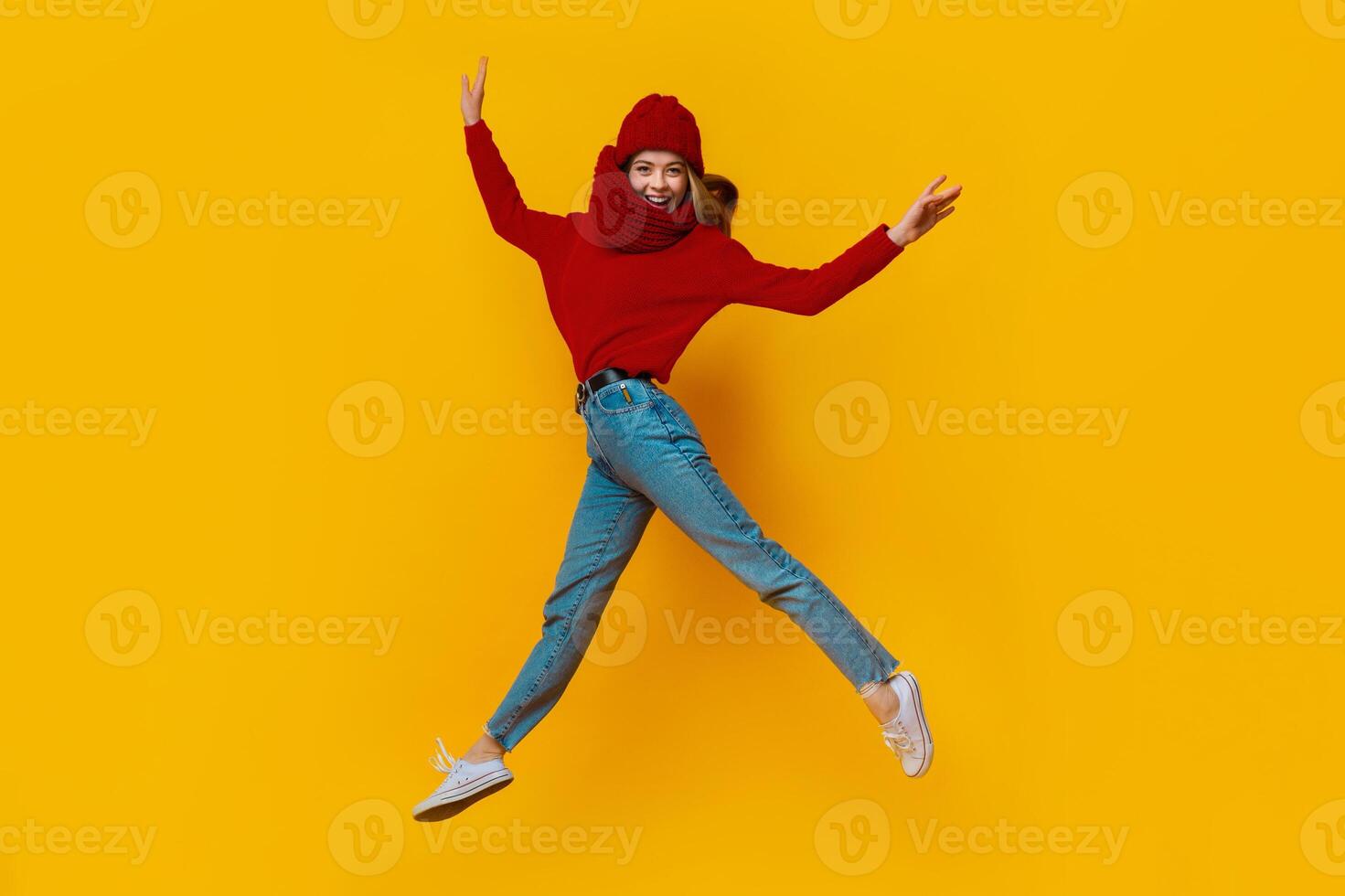 Happy pretty girl in winter hat and scarf showing funny moves in the air over yellow background photo
