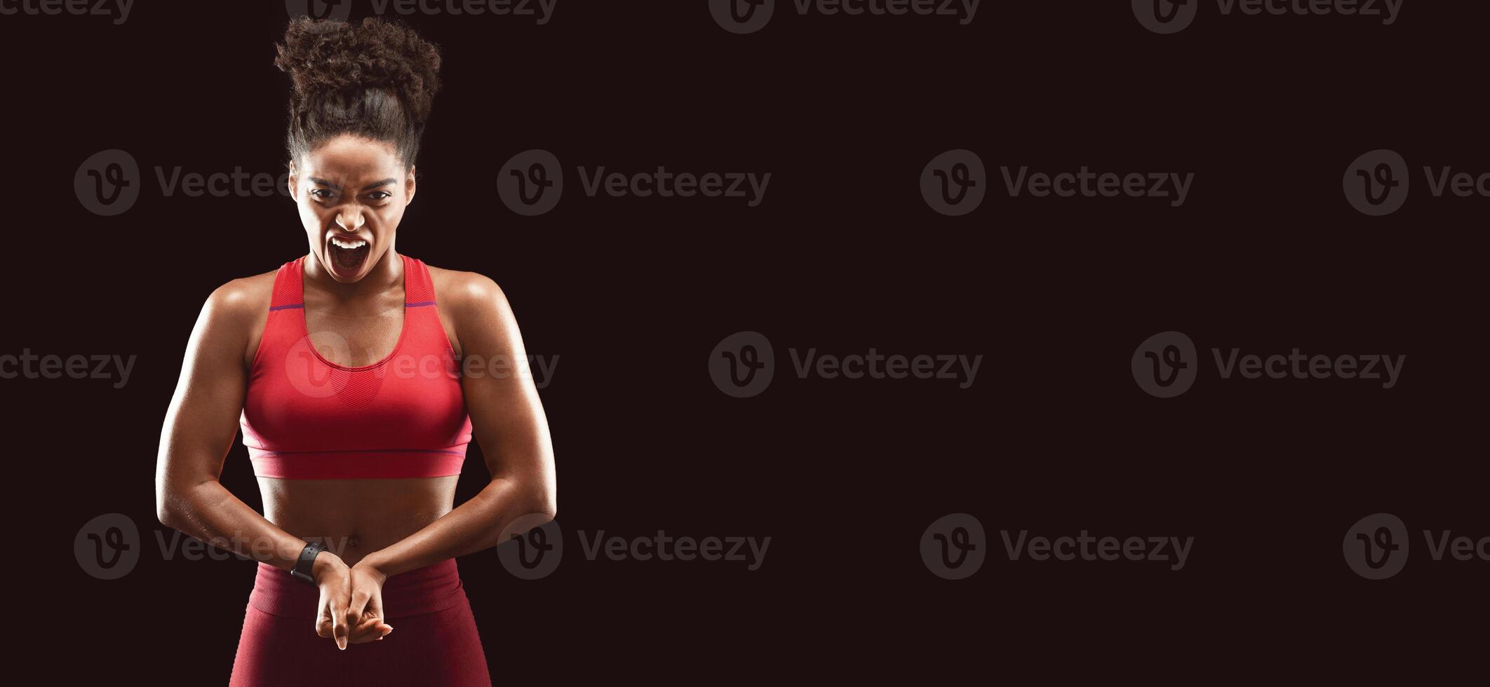 Professional african american female bodybuilder posing on camera, aggressive face expression, showing hands muscles, black studio background photo