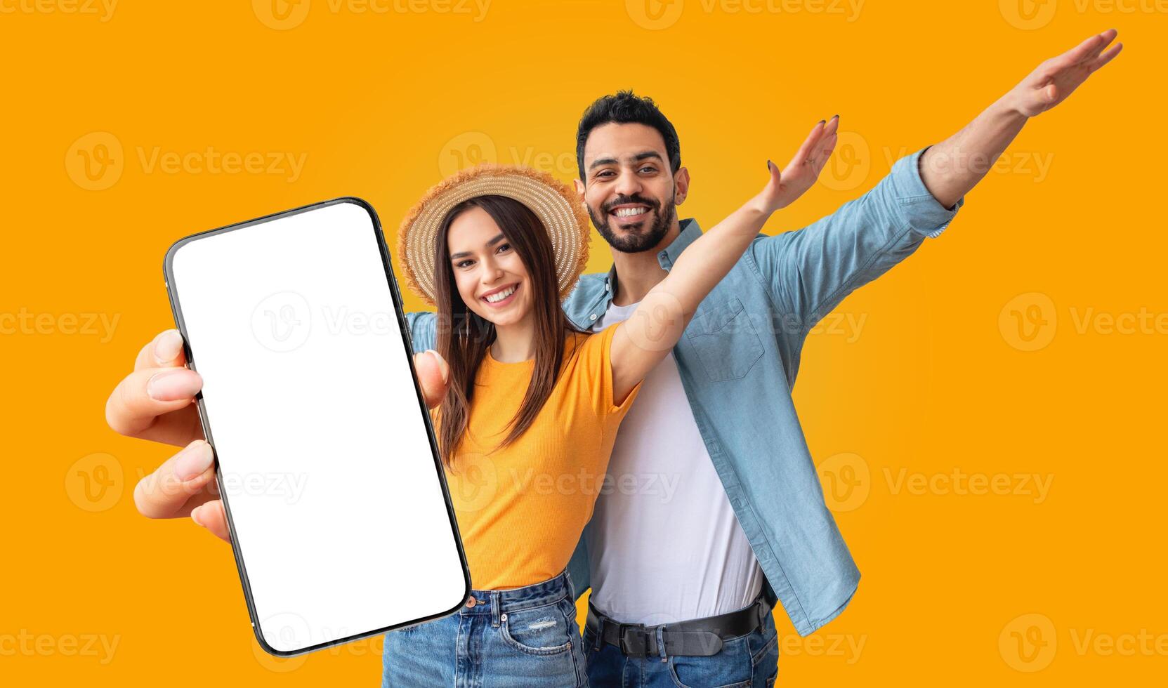 Multiracial couple stands together in front of a bright yellow background. The woman is holding a smartphone with a blank screen photo