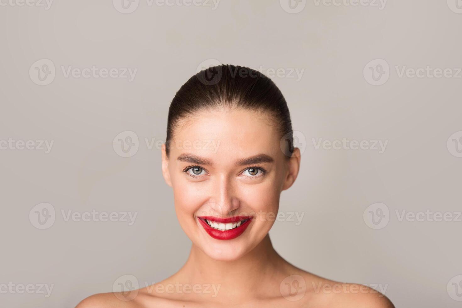 A beautiful half-naked woman showcasing red lipstick on a neutral gray background. Her features are highlighted, focusing on the bold lip color against the muted backdrop. photo