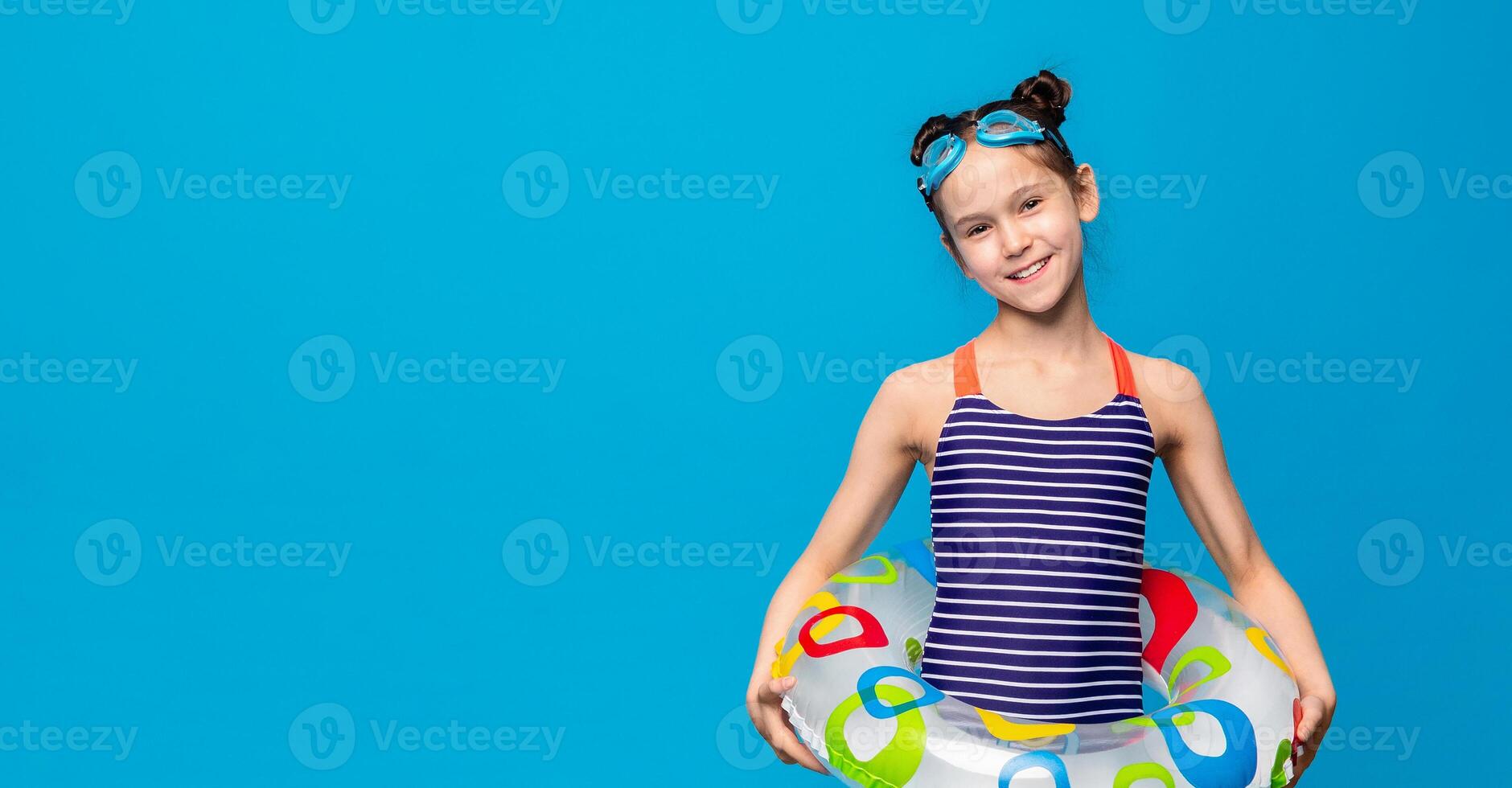 A young girl wearing a blue and white striped swimsuit is seen holding a large inflatable float. She appears to be enjoying a day at the pool or beach, copy space photo