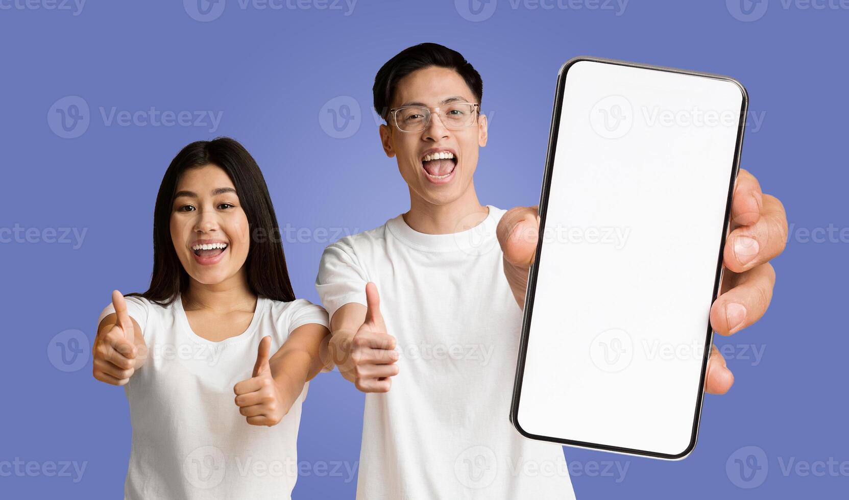 Asian man and woman are both smiling and giving a thumbs up while standing in front of a purple background. The man is holding a smartphone with a blank screen, showcasing its features photo