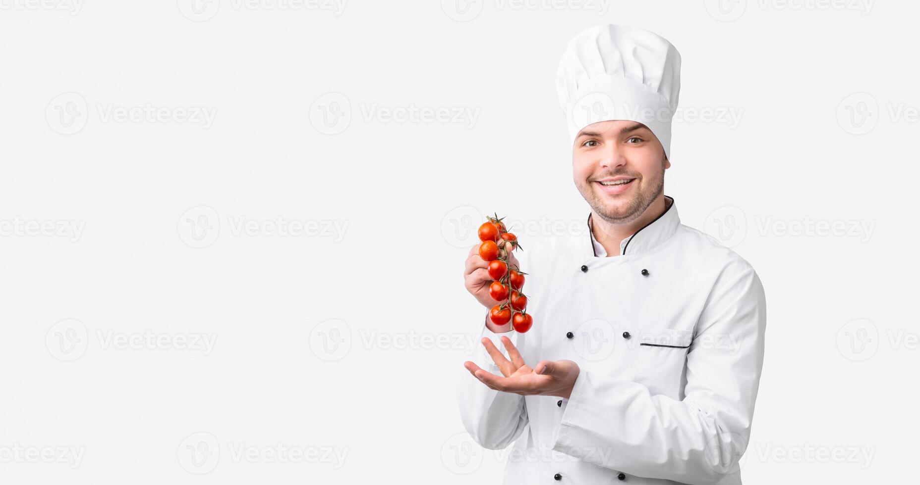 sonriente cocinero hombre participación Cereza Tomates rama recomendando comiendo vegetales en pie en blanco estudio antecedentes. panorama foto