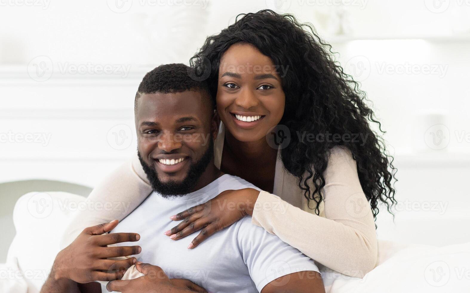 A smiling Black couple embraces indoors, with the womans arm around the mans shoulder. photo