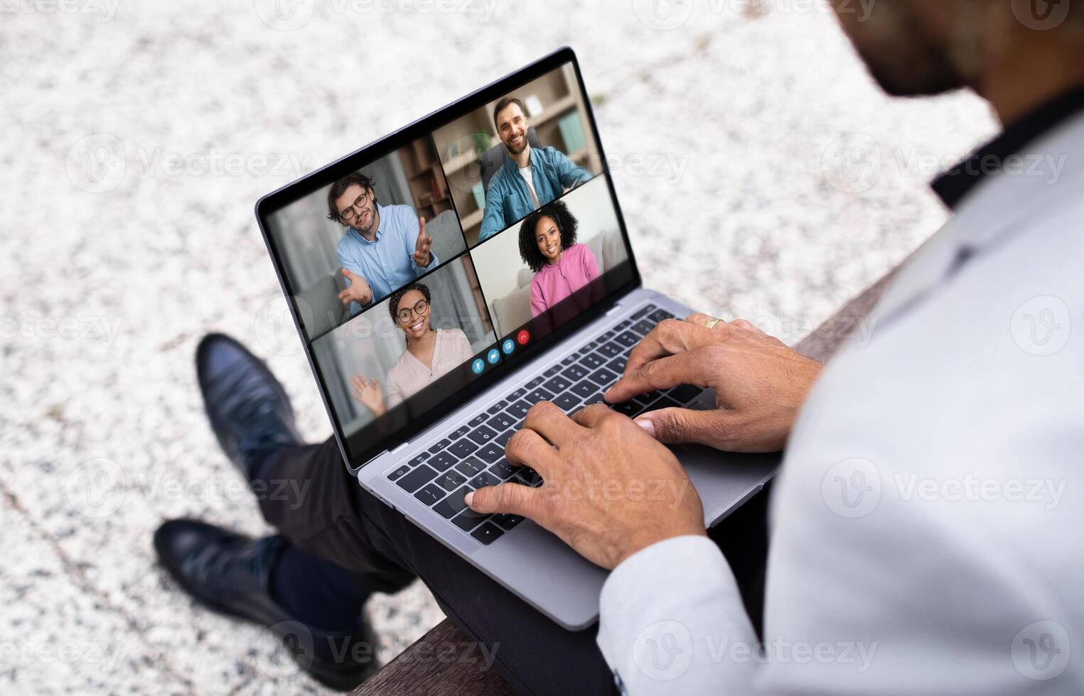 A businessman is participating in a conference call on his laptop while sitting outdoors in an urban environment. Five colleagues appear on the screen in a professional, virtual meeting. photo