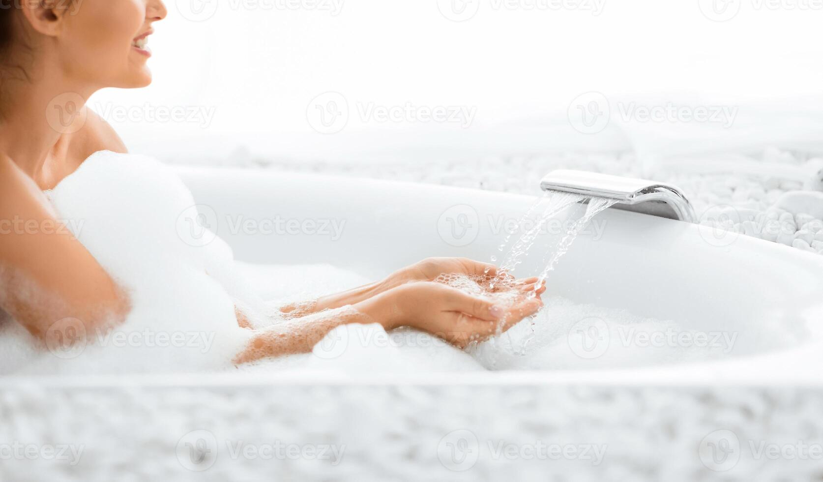 Perfect morning. Woman making bubble bath and checking temperature of running water photo