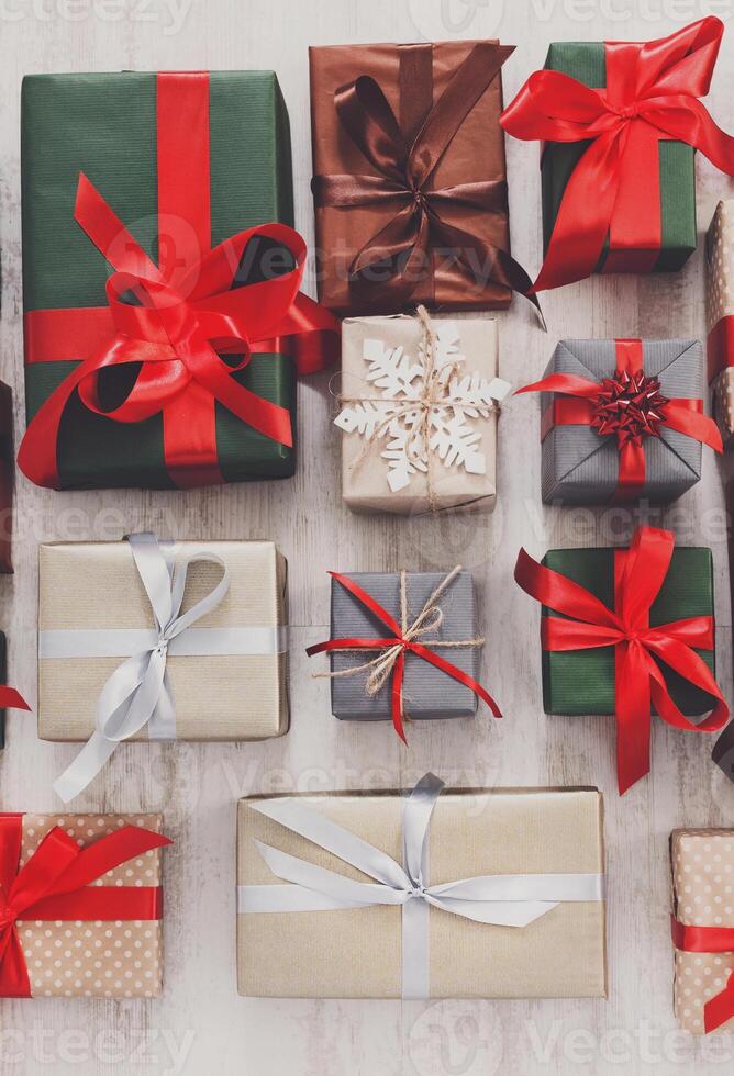 Lots of Gift boxes on white rustic wood background. Presents in craft and colored paper decorated with red satin ribbon bows. Christmas and other holidays concept. Top view, flat lay photo