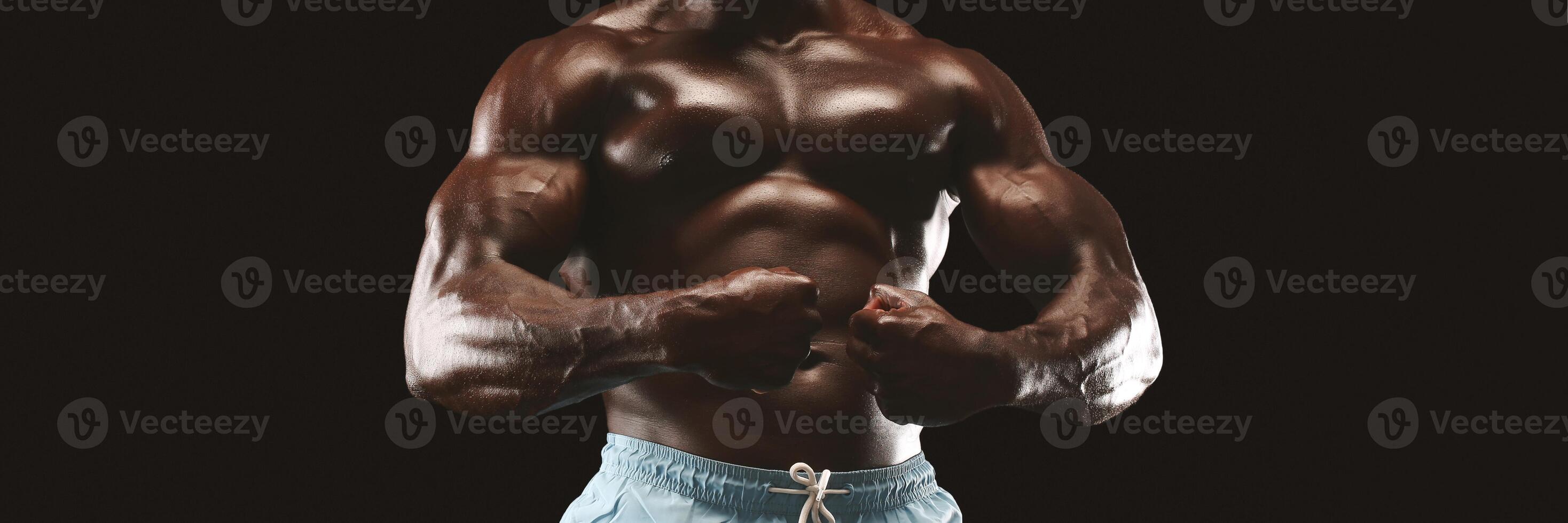 A muscular man flexes his biceps in front of a black background. photo
