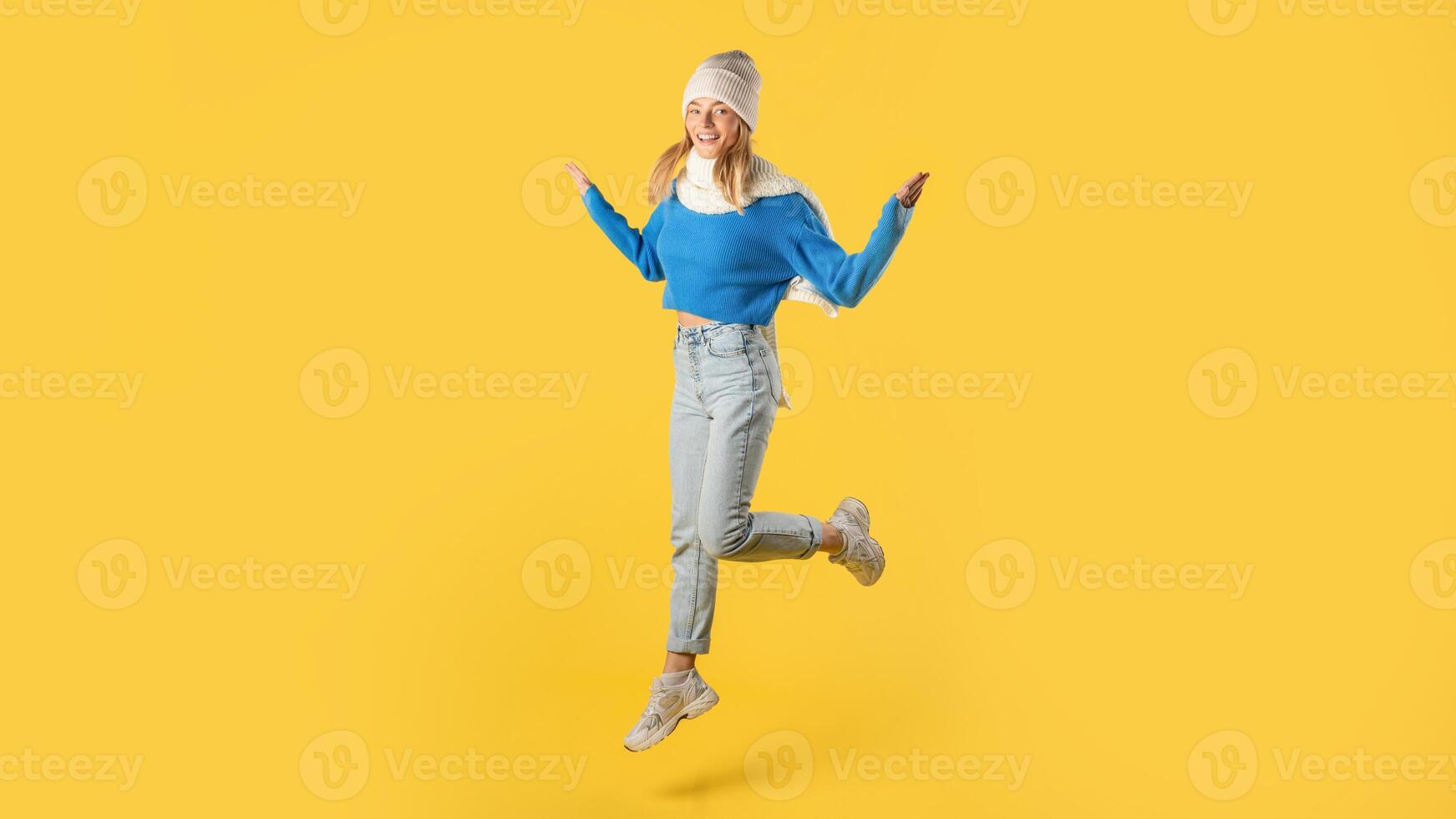 A woman wearing a blue sweater is captured mid-air as she jumps energetically. Her expression shows joy and freedom as she defies gravity in her casual attire. photo