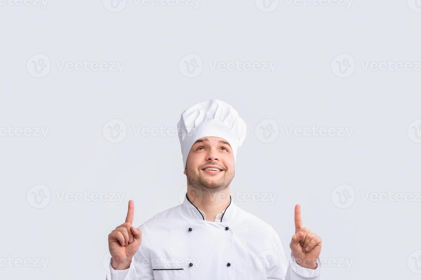 Look Up. Positive Chef Guy Pointing Fingers Upward Standing Over White Studio Background. Panorama photo