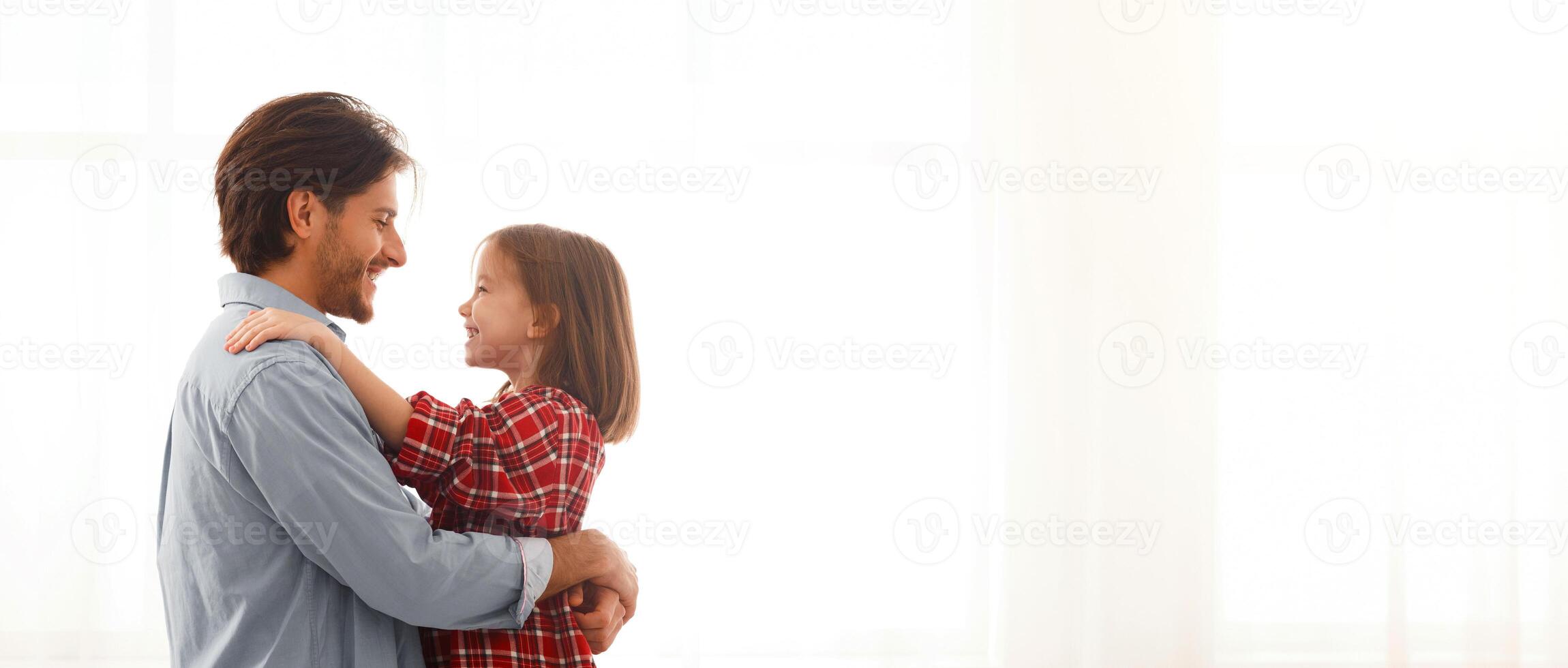 Daddy and daughter looking at each other and hugging over big window at home, copy space photo
