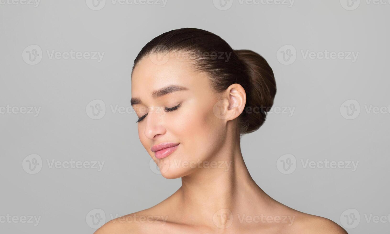 A woman is depicted with her eyes closed against a plain gray background. She appears serene and introspective, possibly lost in thought or meditation. photo