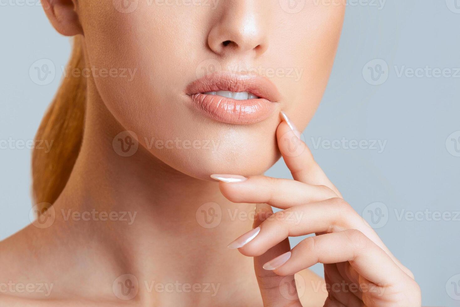 This image shows a close-up of a woman face and hand against a light blue background. The image focuses on the woman lips, chin, and hand resting on her cheek, cropped photo