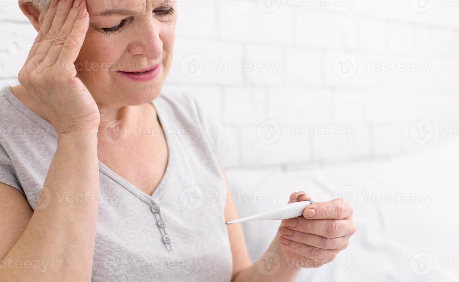 Senior woman is seen holding a thermometer in her hand, likely checking her temperature for any signs of fever or illness, closeup photo