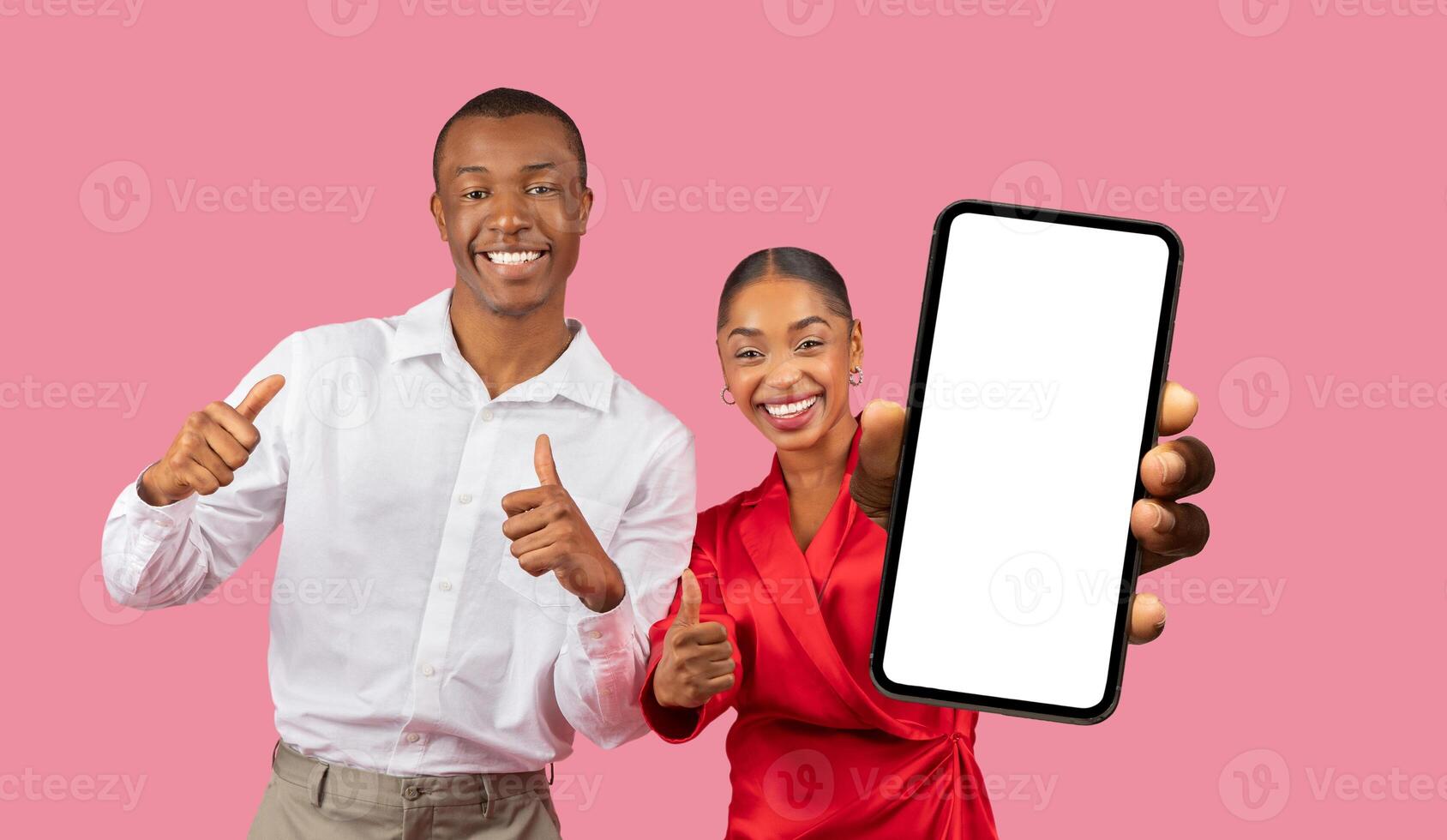 This image features a happy African American couple standing in front of a pink background. The woman is holding a smartphone with a blank screen in front of her, while the man is giving a thumbs-up photo