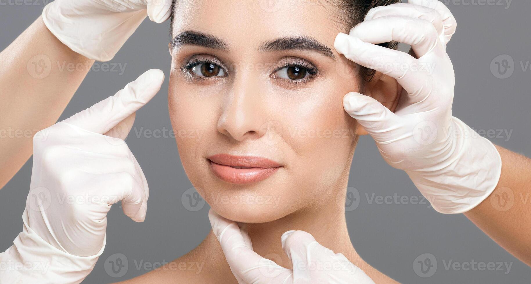 Medical professionals wearing gloves assess a woman facial skin by gently touching and inspecting different areas. The focus is on her clear and glowing complexion. photo