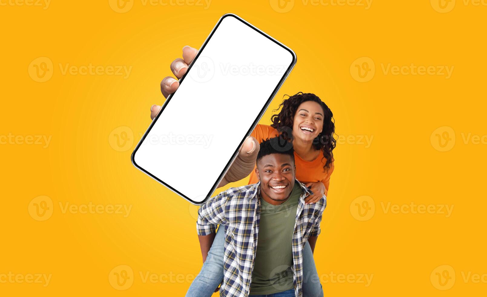 African American young couple is smiling and looking at the camera, woman holds a large smartphone with a blank screen in front of them photo