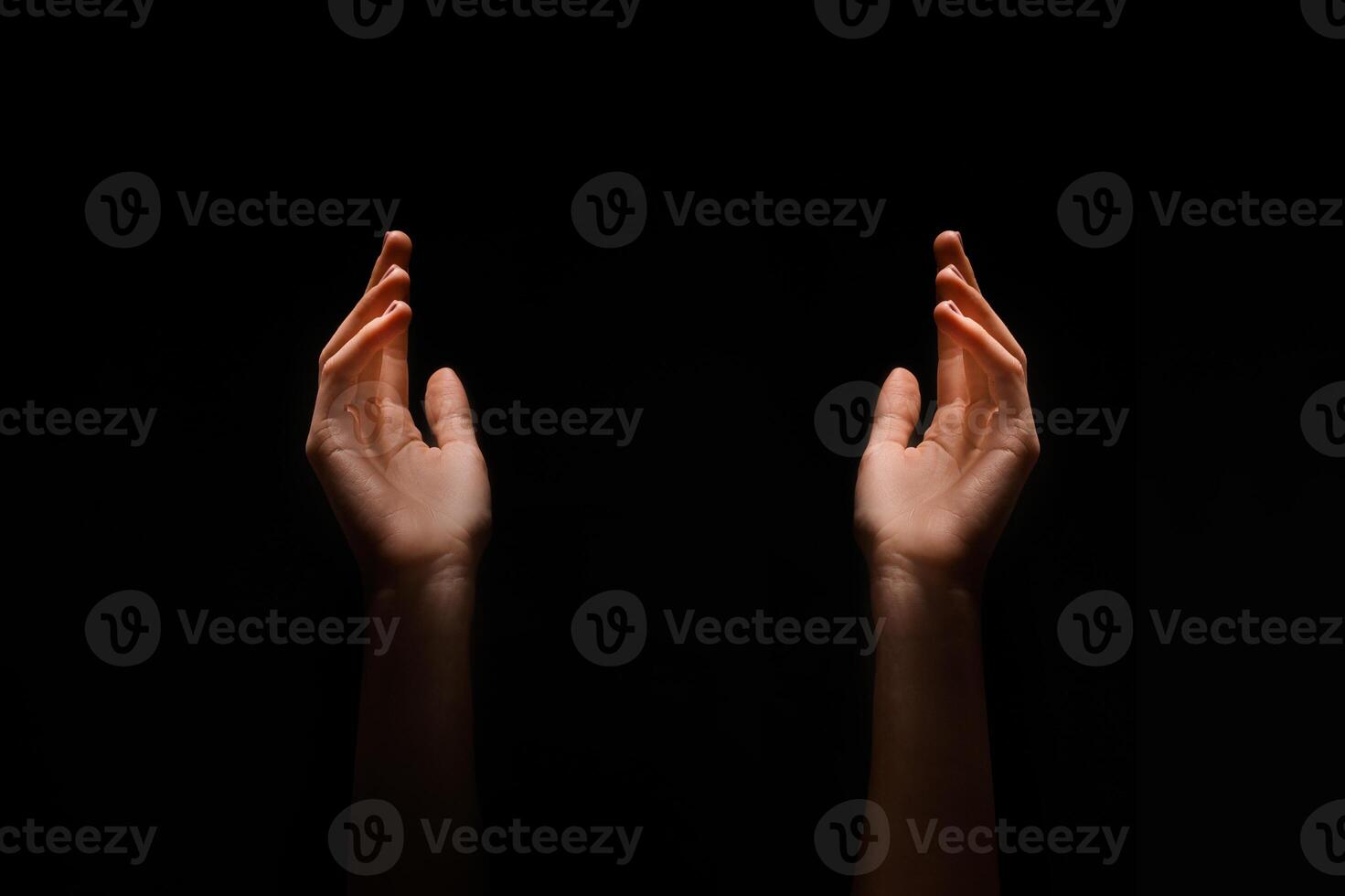 This image shows two hands reaching upward in the dark. The hands are positioned symmetrically, with their palms facing upwards. photo