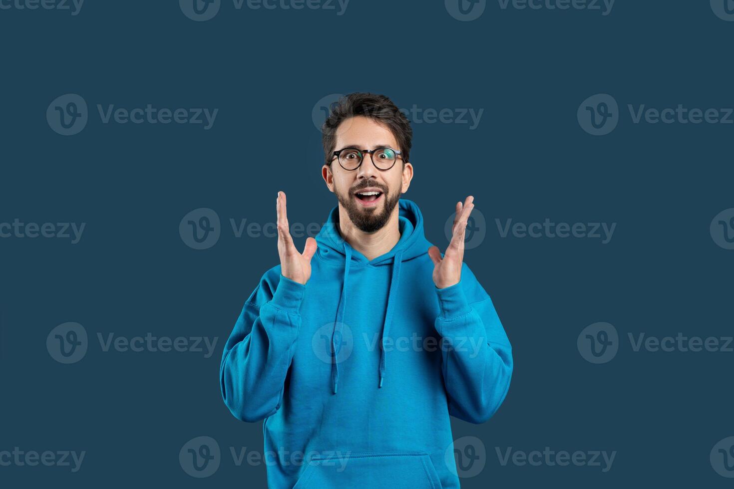 A man wearing a blue hoodie is seen gesturing with his hand in this photograph. The gesture appears to be deliberate and expressive, drawing attention to his actions. photo