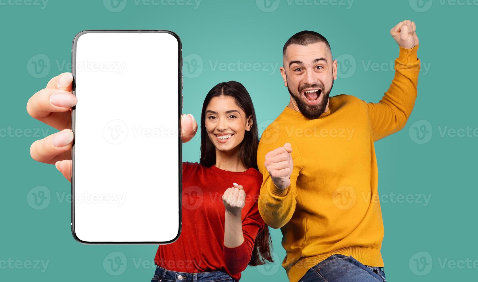 A young couple celebrates their success with big smiles and excited gestures. The woman is holding a smartphone with a blank screen, while the man is raising his fist in the air. photo