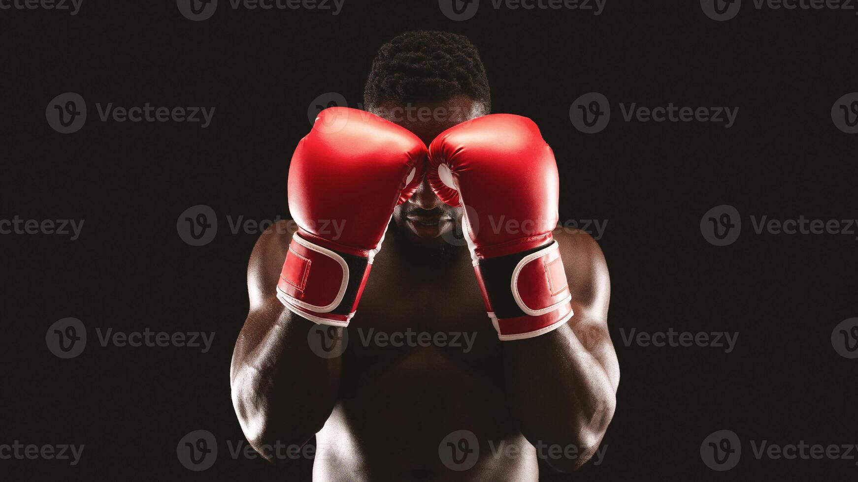 A boxer stands with his red gloves raised to his face, ready for a fight. photo